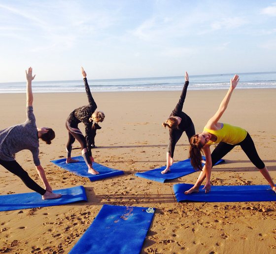 Small group practising yoga on mats on a sandy beach