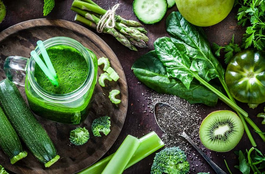 Green smoothie surrounded by spinach, broccoli, kiwi and cucumber